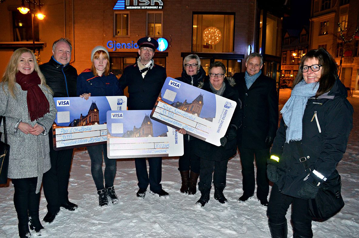 Gruppebilde av mennesker med gavesjekker og gavemottakere utenfor gamle Harstad Sparebank.